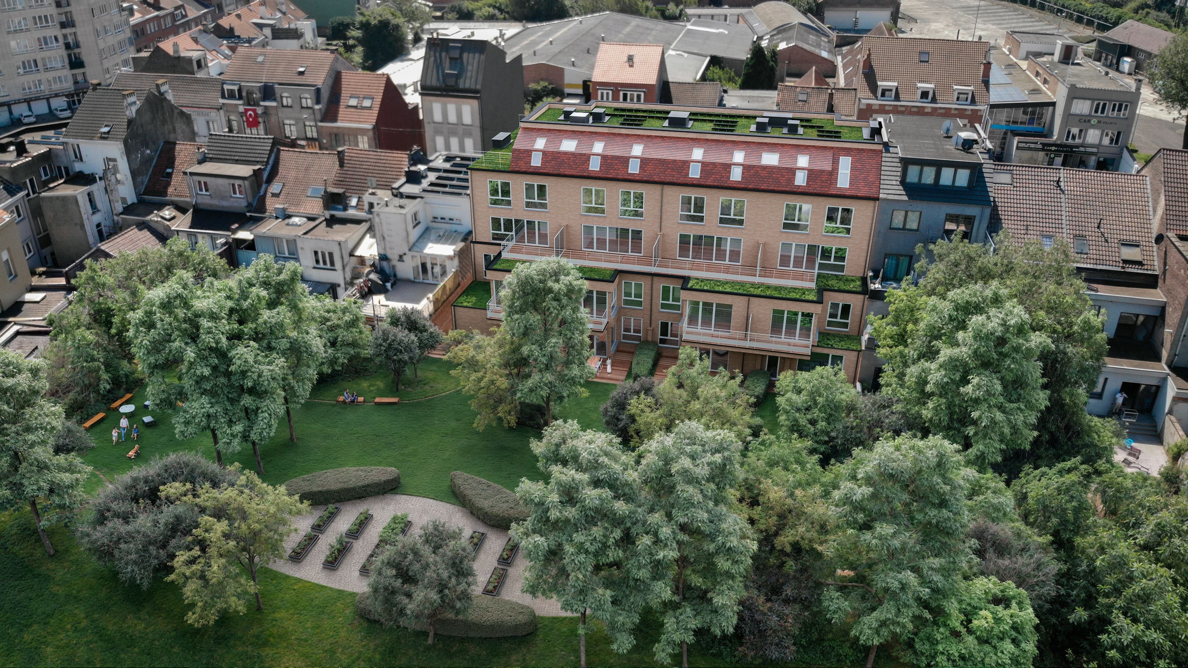 Vue aérienne d'un immeuble résidentiel neuf avec toiture verte et grands balcons, donnant sur un jardin commun arboré et aménagé en plein cœur de Bruxelles.
